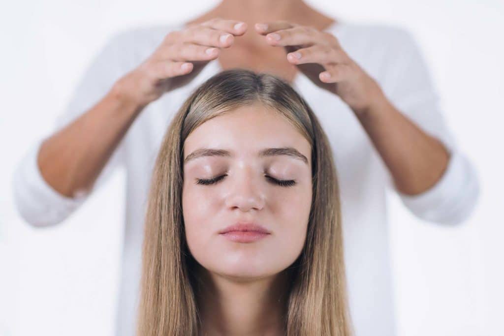 una maestra reiki coloca sus manos en la cabeza de una paciente joven